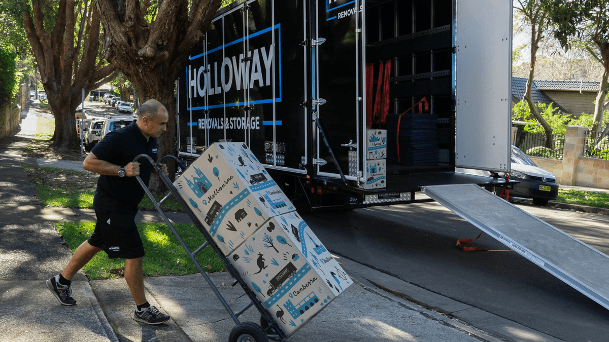 man pushing a trolley stacked will boxes into a holloway removals moving truck