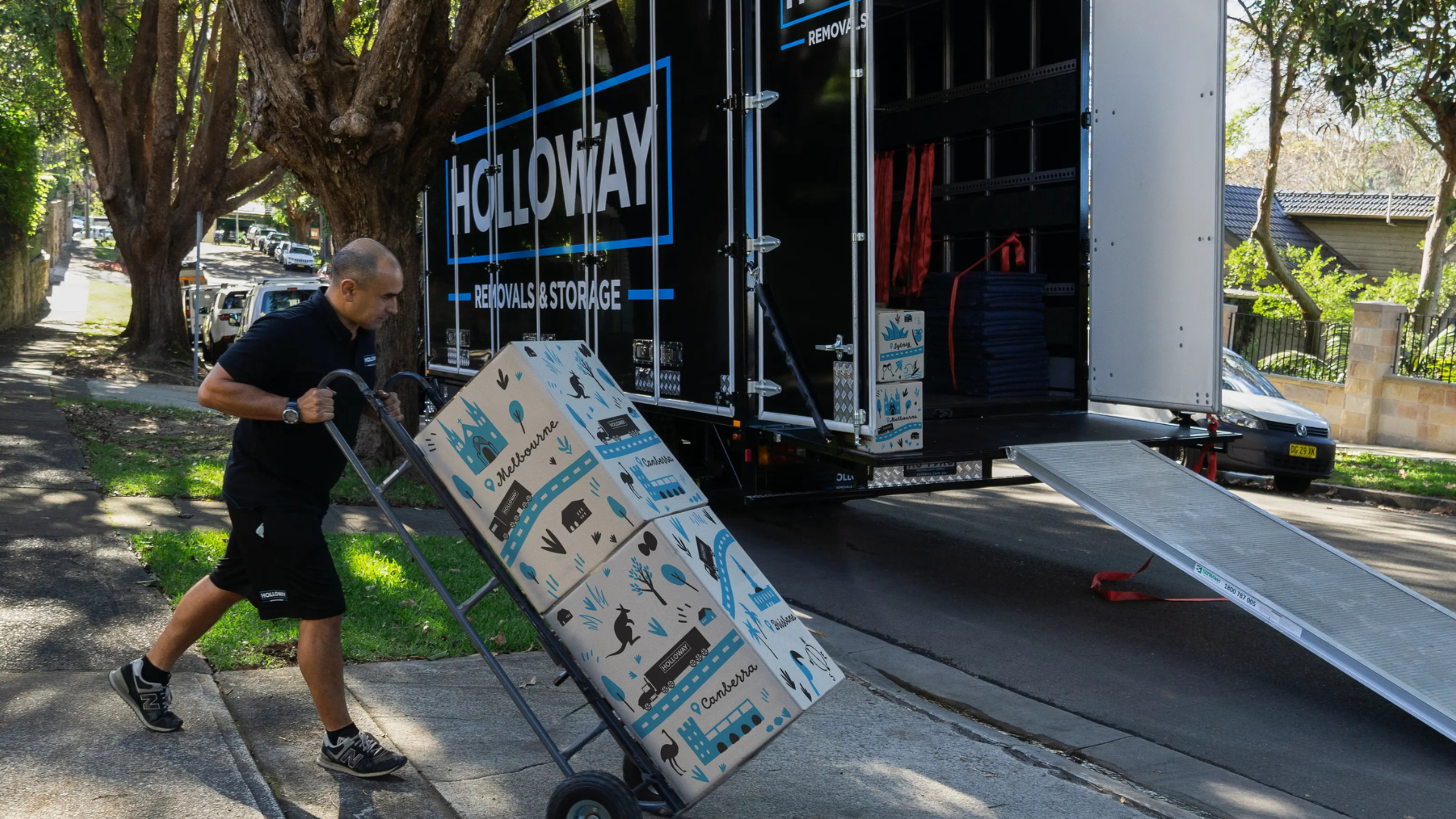 man pushing a trolley stacked will boxes into a holloway removals moving truck
