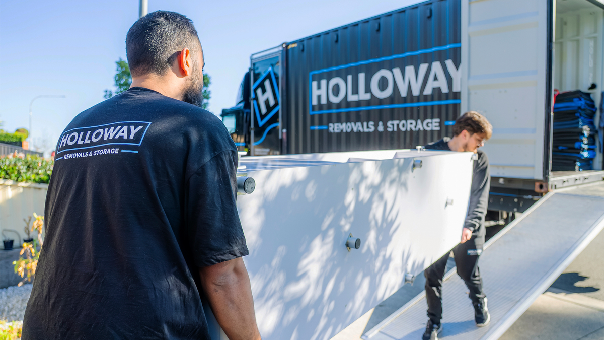 Two Holloway removalists carrying a large heavy item up a truck ramp during a professional move