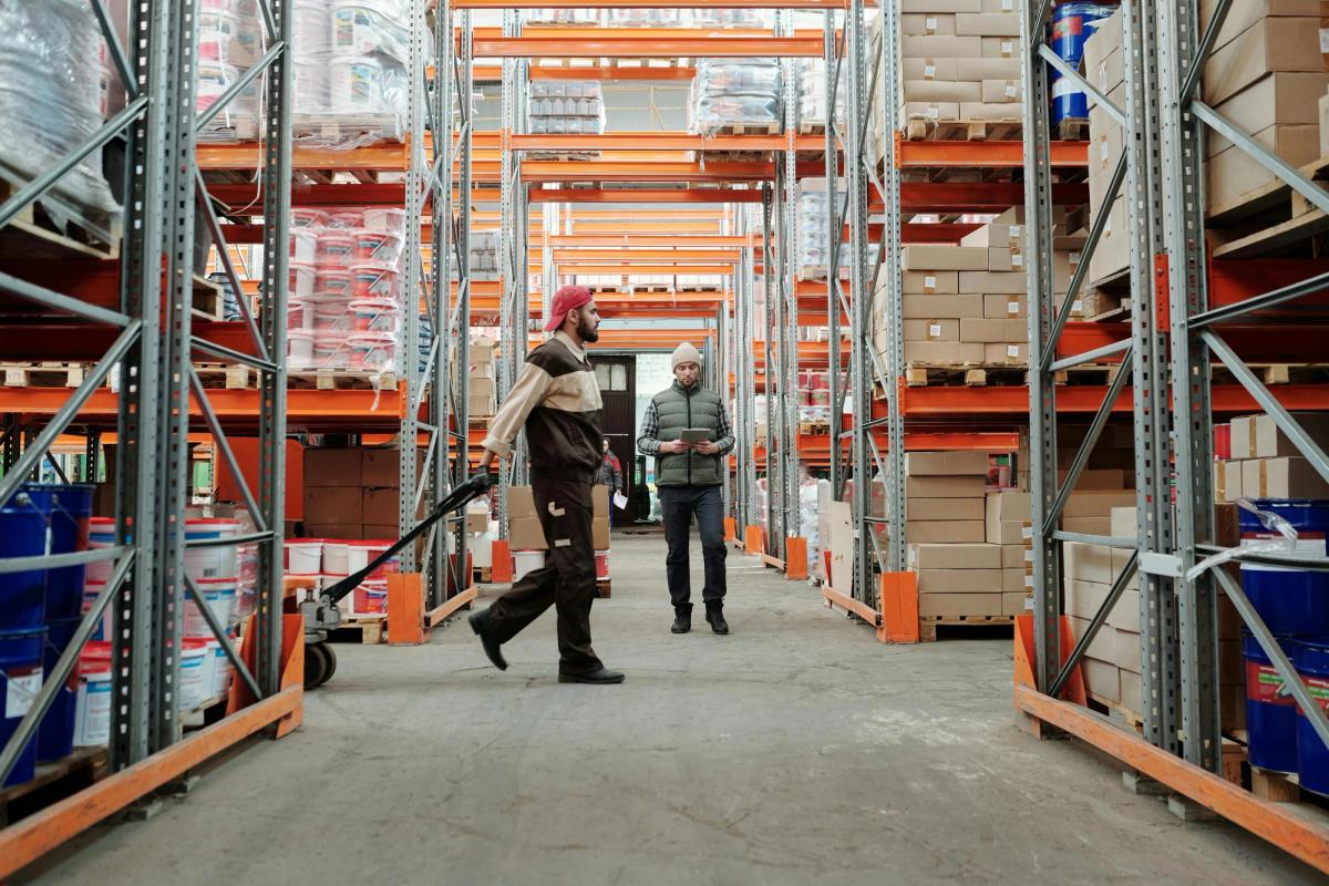 man walking through a storage warehouse pulling a trolley