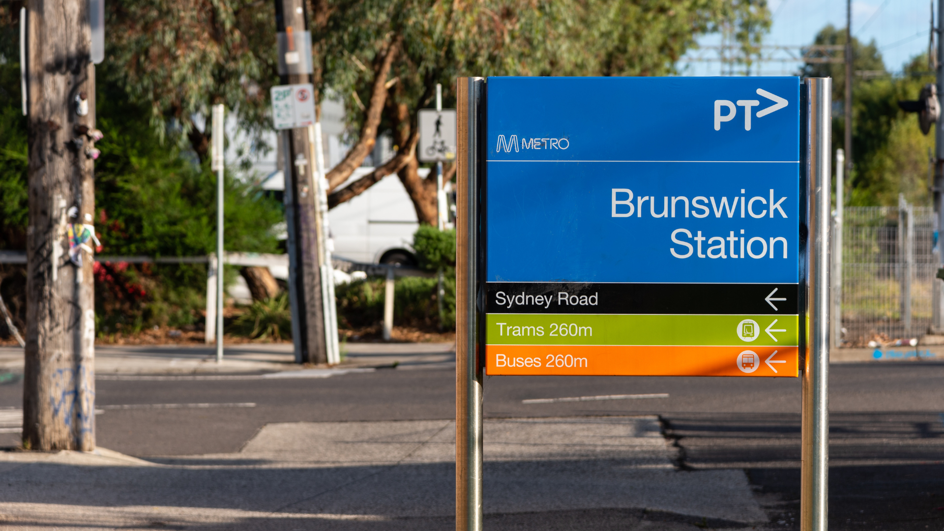 A blue PTV station sign for Brunswick Station showing directions to Sydney Road, trams, and buses