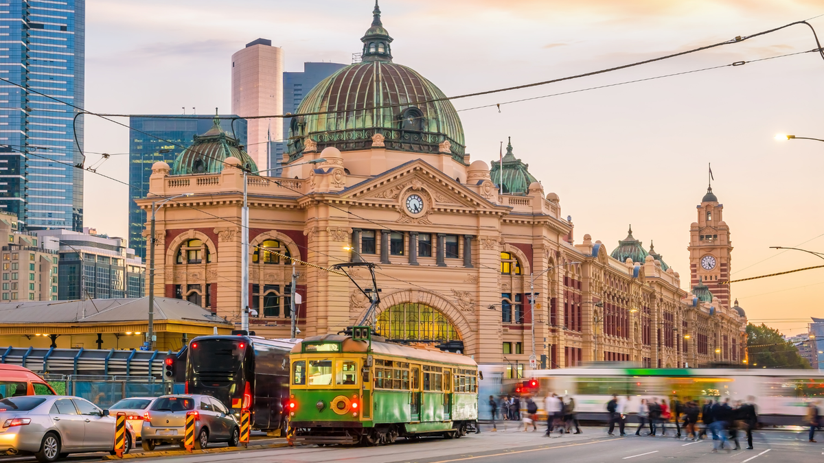 Iconic flinders street station in Melbourne with a green vintage tram and city skyscrapers at sunset