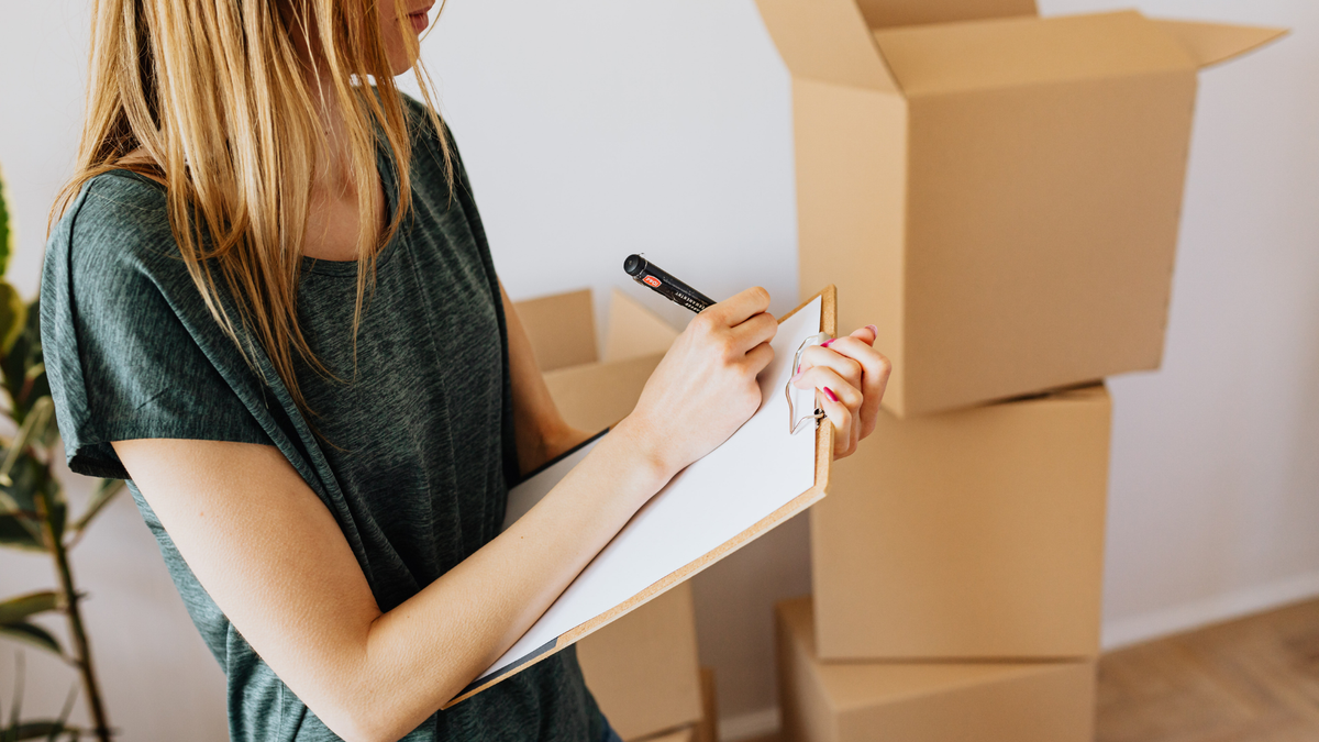 Woman writing a storage inventory checklist next to moving boxes
